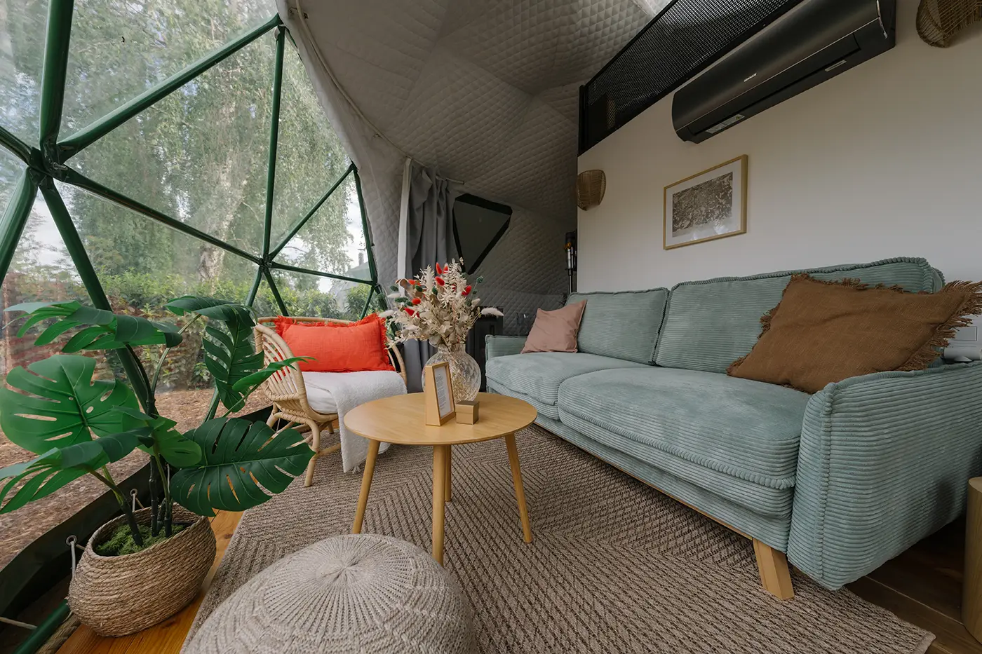 Dome living area with a green corduroy sofa, a round wooden coffee table with flowers and a potted plant by the glass facade